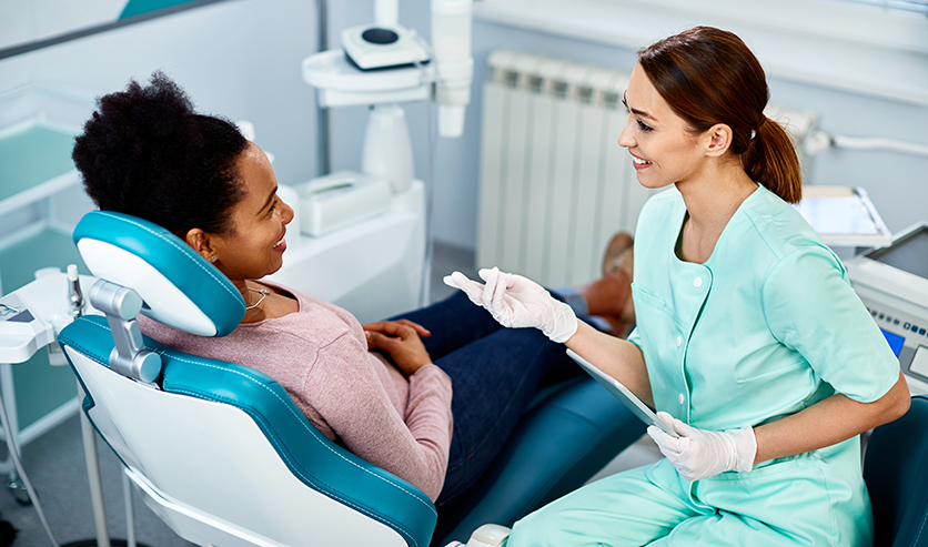 A womnan sitting in a dentist's chair chats to the dentist