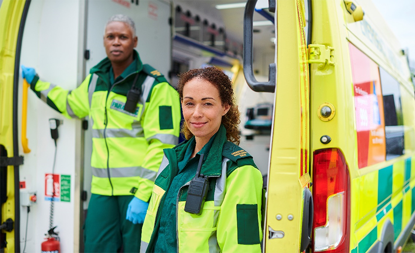 An ambulanceman and an ambulancewoman standing in front of their ambulance