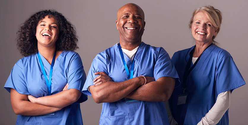 Two female and one male nurse standing next to each other, looking straigh ahead, laughing