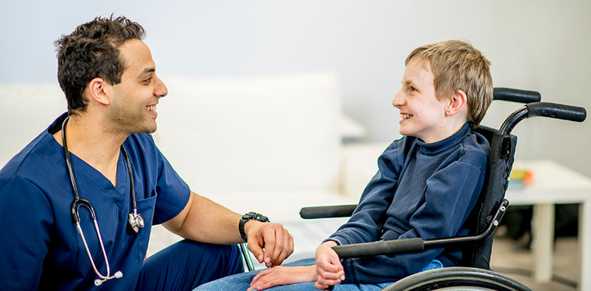 A male nurse kneels down to talk to a boy who is in a wheelchair