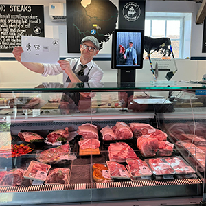 A butcher at his meat counter holding a Makaton symbols board